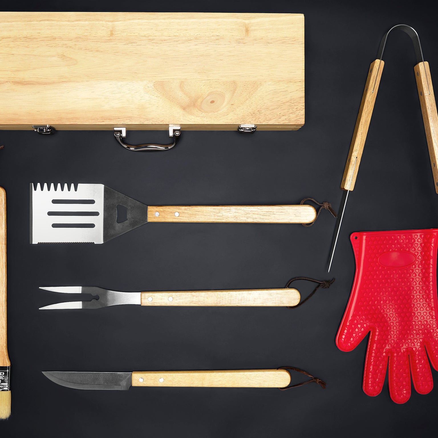 Wooden BBQ grilling tool set with stainless steel utensils, including a spatula, fork, knife, and tongs, laid out next to a red silicone heat-resistant glove on a black background.