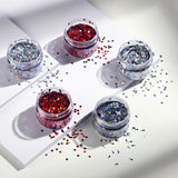 Five small jars of glitter on a white surface with scattered glitter.